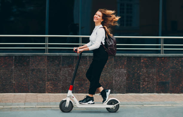 Young woman with smile ride electric scooter at the street stock photo