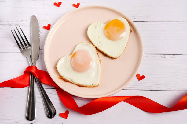 istock Breakfast on Valentine's Day - fried eggs on plate and red hearts on white wooden table. Top view 1294413663