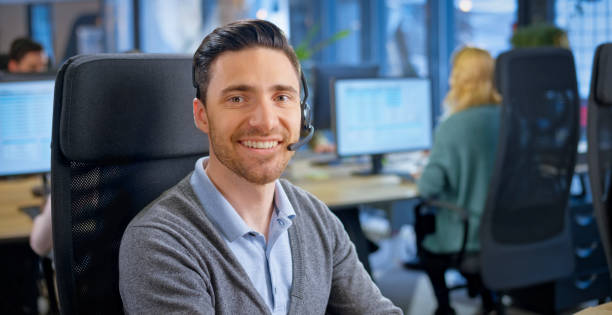 Young man working in call centre Portrait of smiling customer service representative wearing wireless headset working in call centre. real time stock pictures, royalty-free photos & images