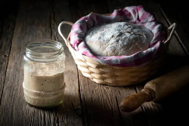 Sourdough glass preparing real bread dough homemade bakery in moody wooden table low key dark background