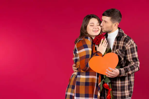 Portrait of a couple inlove on a red background with side space with roses and a big heart in their hands. High quality photo