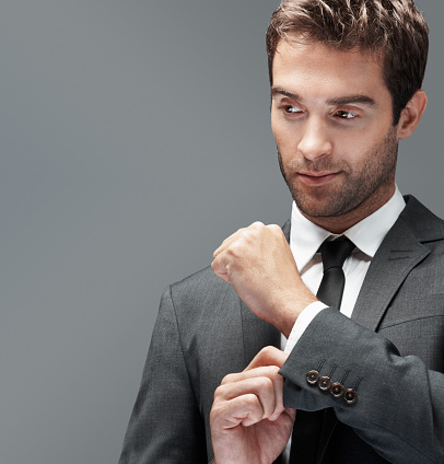 Handsome man looking thoughtfully in to copyspace while doing his cufflink, isolated on grey