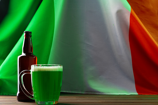Glass of green beer against flag of Ireland close up