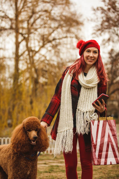 istock Young woman using her phone while walking her cute poodle 1294426231