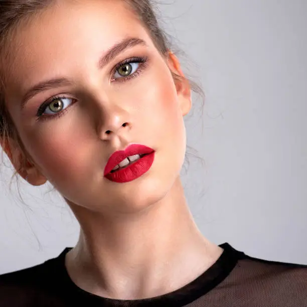 Beautiful thin girl with brown hair. Fashion model posing in the studio.  Attractive woman with bright make up looking at the camera. Pretty caucasian girl with a tilted head and red lipstick.