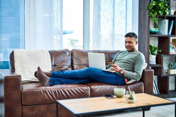 Less queues, more convenience Shot of a man using a laptop and credit card on the sofa at home Convenience stock pictures, royalty-free photos & images