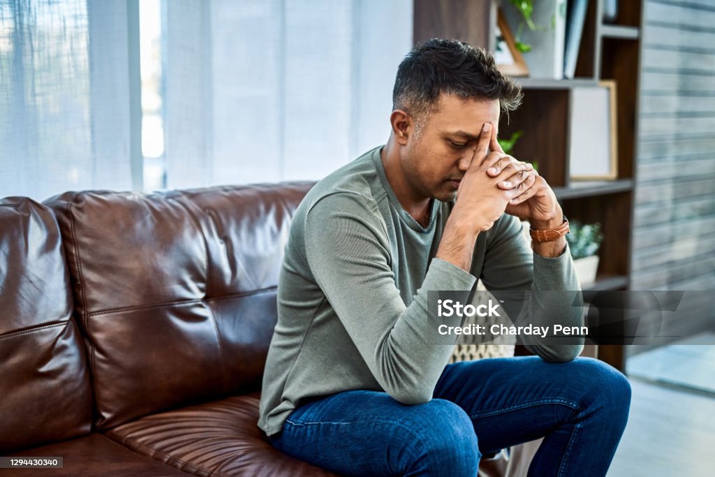 It's okay to ask for help with your mental health Shot of a man looking stressed while sitting on the sofa at home Men Stock Photo