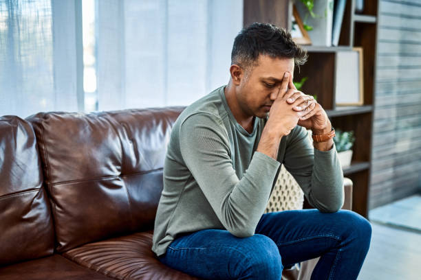 It's okay to ask for help with your mental health Shot of a man looking stressed while sitting on the sofa at home emotional stress stock pictures, royalty-free photos & images