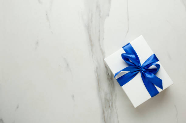 istock Top view of white box and blue ribbon, bow on the empty marble table.Present box 1294430778