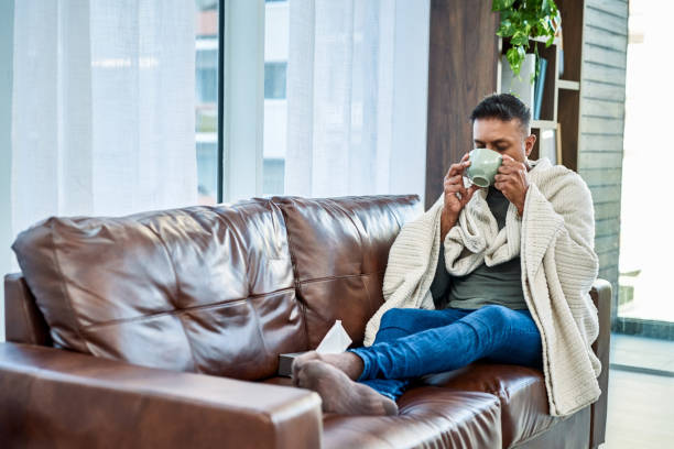 Do what you've gotta do to recover from the flu Shot of a man having a warm drink while recovering from an illness on the sofa at home cold and flu man stock pictures, royalty-free photos & images