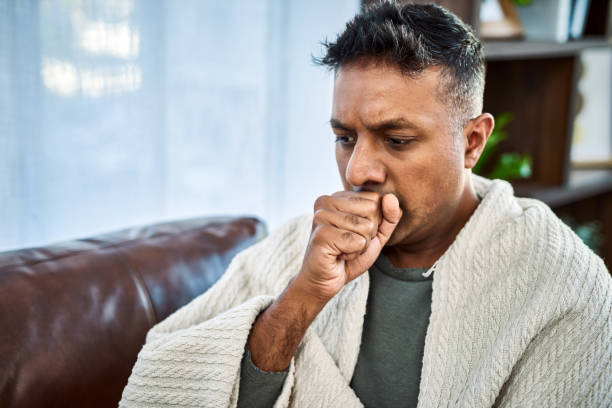 What kind of cough is this? Shot of a man coughing while recovering from an illness on the sofa at home bronchitis stock pictures, royalty-free photos & images