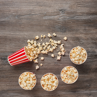 Top view of five paper cups with red stripes and popcorn, on a beautiful wooden background.