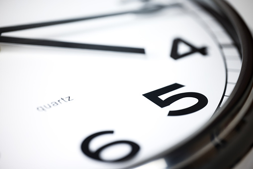 A Modern white wall clock with aluminium frame. Close up to a wall clock, the pointers at quarter pass 4. Selective focus on the number 5 or 5 o'clock. Reflections in the aluminum frame of the watch.