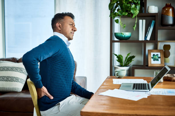 I might need a new chair Shot of a businessman suffering from back pain while working at home posture photos stock pictures, royalty-free photos & images