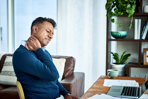 Shot of a businessman suffering from neck pain while working at home