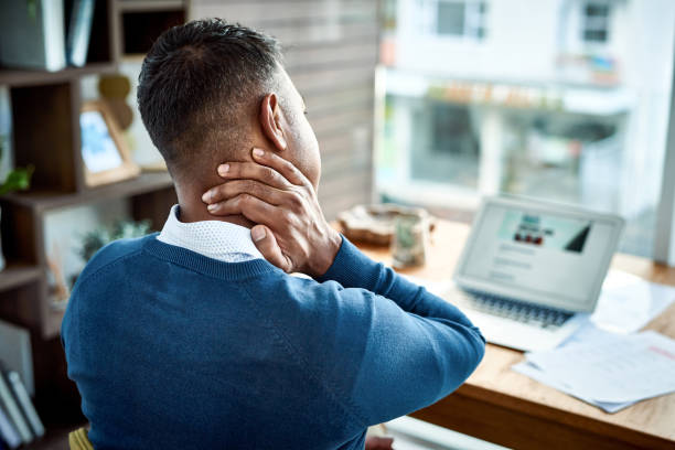 My neck never felt like this at the office Shot of a businessman suffering from neck pain while working at home man in the desk back view stock pictures, royalty-free photos & images