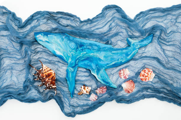 Resin art blue whale with fabric and sea shells on white background. Flat lay, top view