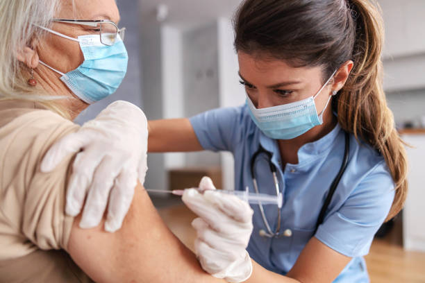 nurse with face mask sitting at home with senior woman and injecting covid 19 vaccine. - injecting flu virus cold and flu doctors office imagens e fotografias de stock