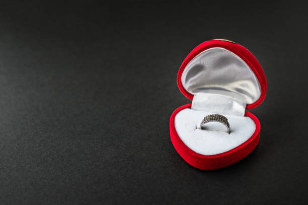 istock Silver engagement ring in red heart-shaped velvet box. Accessory with gems. Romantic gift. Precious present. Marriage proposal. Valentine's day, love and wedding concept. Dark black background. 1294443823