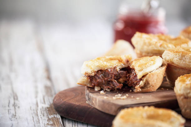 Cut fresh venison meat pies on a rustic wood cutting board Cut fresh venison meat pies on a rustic wood cutting board with filling visible and ketchup in the background. Selective focus on center pie with extreme blurred foreground and background. Free space for text available. meat pie stock pictures, royalty-free photos & images