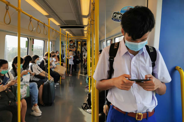 estudiante asiático que usa máscara facial revisando las noticias pandémicas de coronavirus o covic-19 que se sufrías en el tren aéreo. - bangkok mass transit system fotografías e imágenes de stock