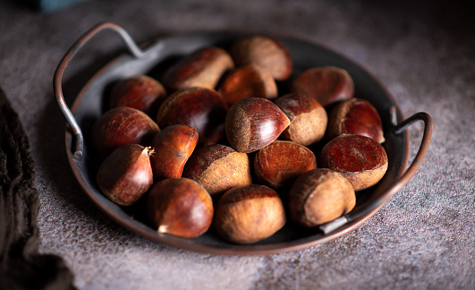 Raw chestnuts on a artistic metal plate in a rustic dark setup