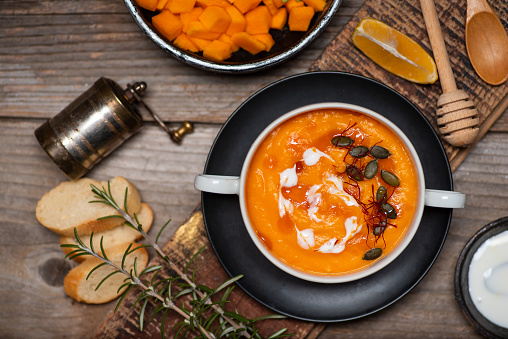 Pumpkin soup on a plate served on rustic wooden table with food ingredients top view