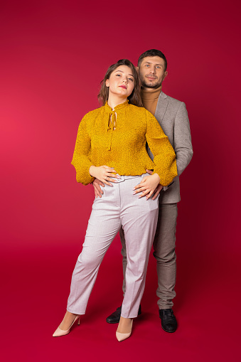Awesome couple in love on st.valentine's day. The man hugs the woman and looks into the camera. Red background. High quality photo