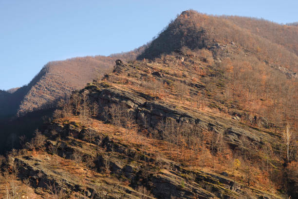 istock Pointy peak, steep, layered cliffs covered by autumn colored trees and clear blue sky 1294458657
