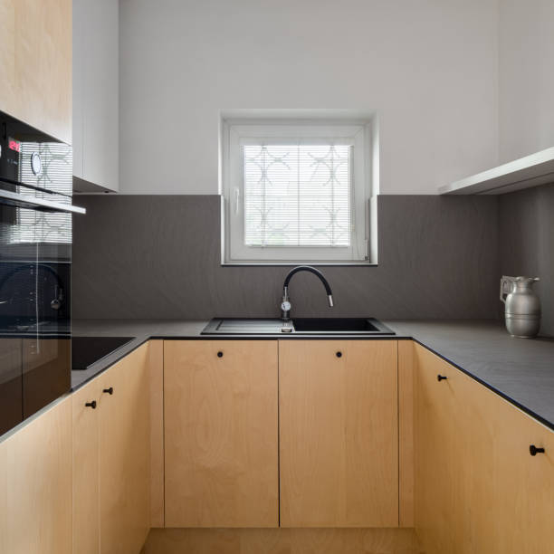Modern kitchen with small window Modern kitchen with birch plywood on cupboards, dark veneer countertops, black sink and tap and small, square window birch wood kitchen worktops stock pictures, royalty-free photos & images