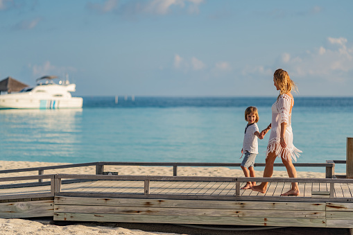 Mother and son walking on beach pier holding hands