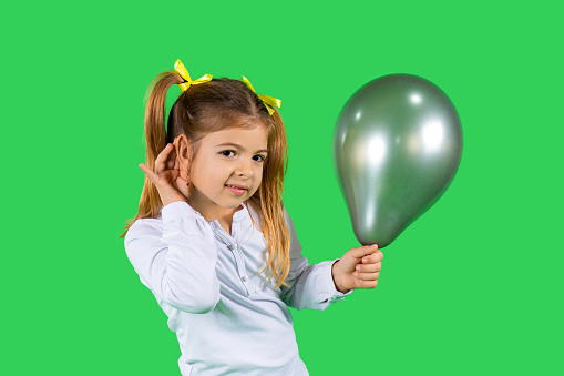 A blond child holding a ultimate gray balloon, with her hand to ear listening to your advertisement. High quality photo