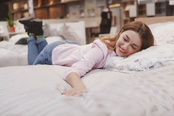 Attractive female customer trying new bed at furniture store, lying comfortably