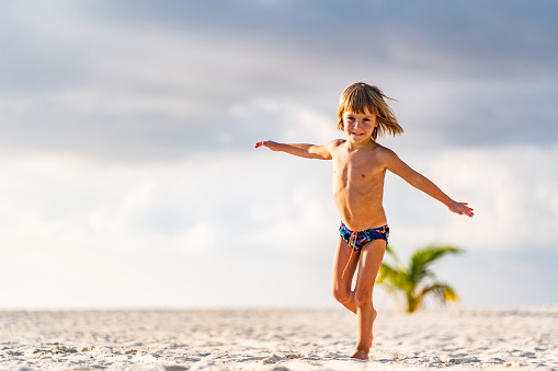 Little boy with arms outstretched running around beach