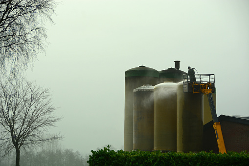 Netherlands,Noorth brabant; january 2 ,2021. Adult men standing on top of a platform. Cleaning with a high-pressure cleaner the agriculture Silo.