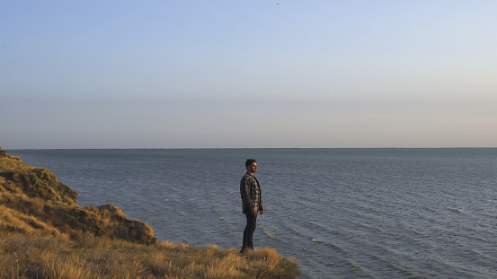 The man stands on the mountain edge on the seascape background