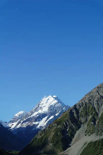 Snow-capped Mount Cook rises between slopes of Southern Alps under clear blue sky.