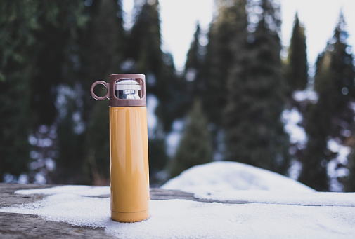 Yellow thermos on wooden table in winter outdoor.