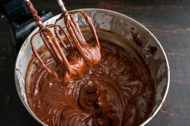 Pastry chef whips melted chocolate in a bowl with a metal wire whisk close up
