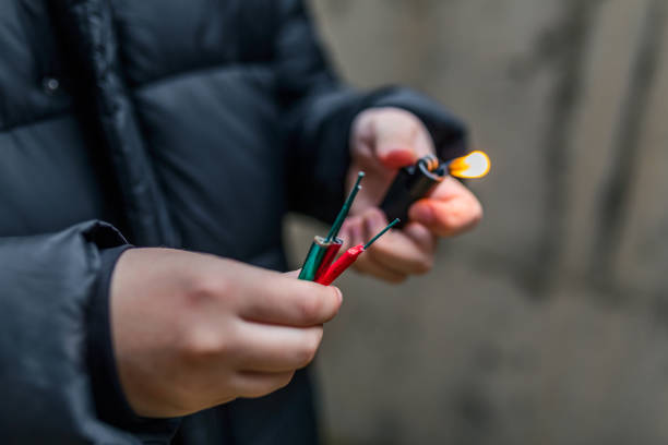 garçon allumant plusieurs pétards dans sa main utilisant le briquet. enfant se préparant pour la célébration avec des feux d’artifice ou des produits pyrotechniques. garçon retenant un pétard brûlant dans sa main. fermez-vous vers le haut du proj - firework explosive material photos et images de collection