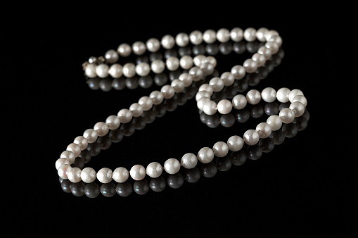 Strand of pearls on a black reflective surface.