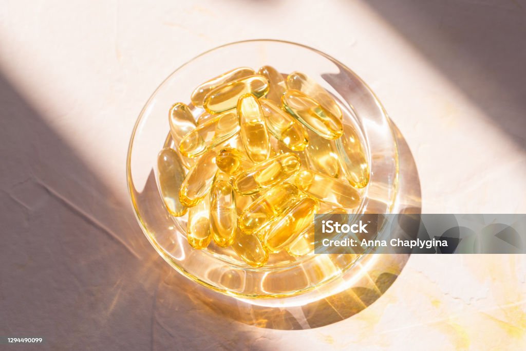 Cod liver fish oil capsules in glass bowl on pink Cod liver fish oil capsules in glass bowl on pink background. Omega 3, Vitamin E supplements. Sunlight and shadows trendy shot. Healthy diet concept. Top view, close up, copy space Omega-3 Stock Photo