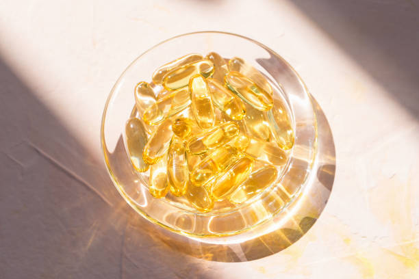 Cod liver fish oil capsules in glass bowl on pink Cod liver fish oil capsules in glass bowl on pink background. Omega 3, Vitamin E supplements. Sunlight and shadows trendy shot. Healthy diet concept. Top view, close up, copy space animal digestive system stock pictures, royalty-free photos & images