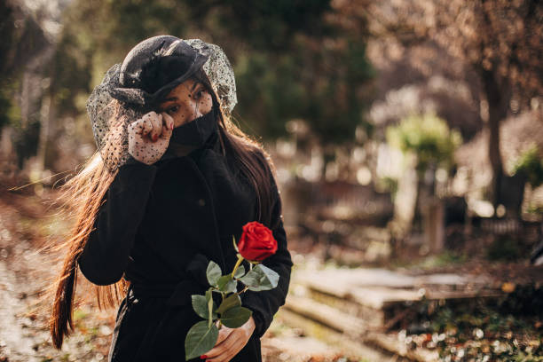 istock One young sad widow with protective face mask carries flowers to a grave 1294498849