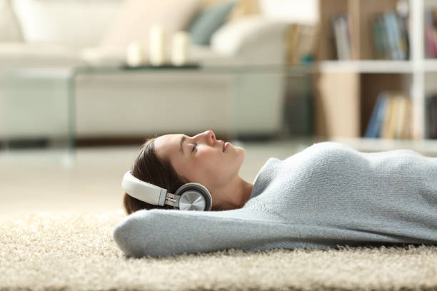 mujer relajada escuchando música con auriculares en casa - descansar fotografías e imágenes de stock