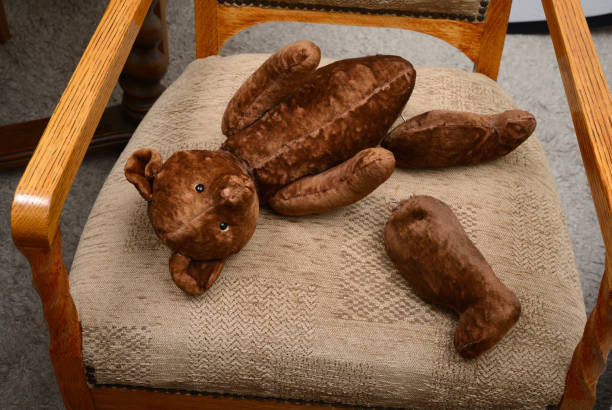 broken teddy bear toy with severed paws on an antique armchair stock photo