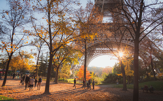 Tourists, locals and families enjoy a scenic autumn stroll as sunlight bursts through the iconic Eiffel Tower in Paris, France.