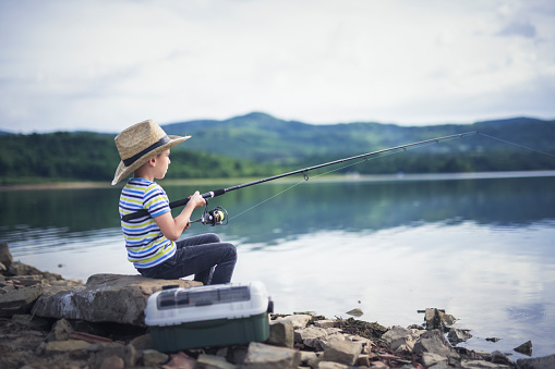 Little boy with straw hat fishing on lake.