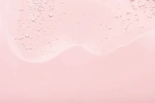 Photo of The texture of the gel, skincare serum on a pink background. A transparent liquid cosmetic with bubbles to moisturize the skin of the face and body. Cleansing beauty product, scrub with natural acids