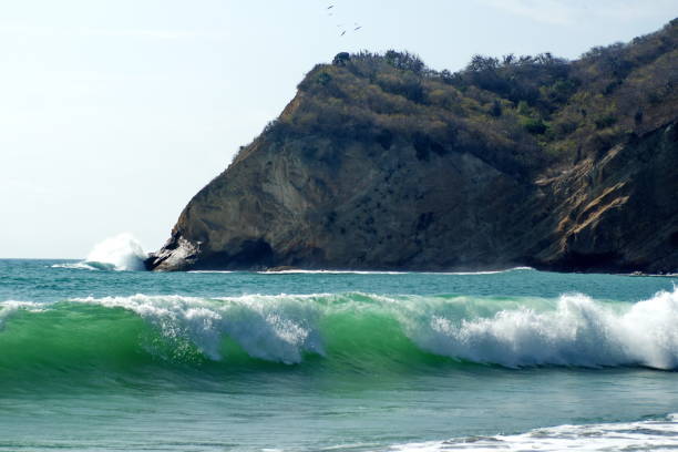 Waves breaking at the shore with a cliff in the background on Los Frailes Beach in Machalilla National Park near Puerto Lopez, Ecuador